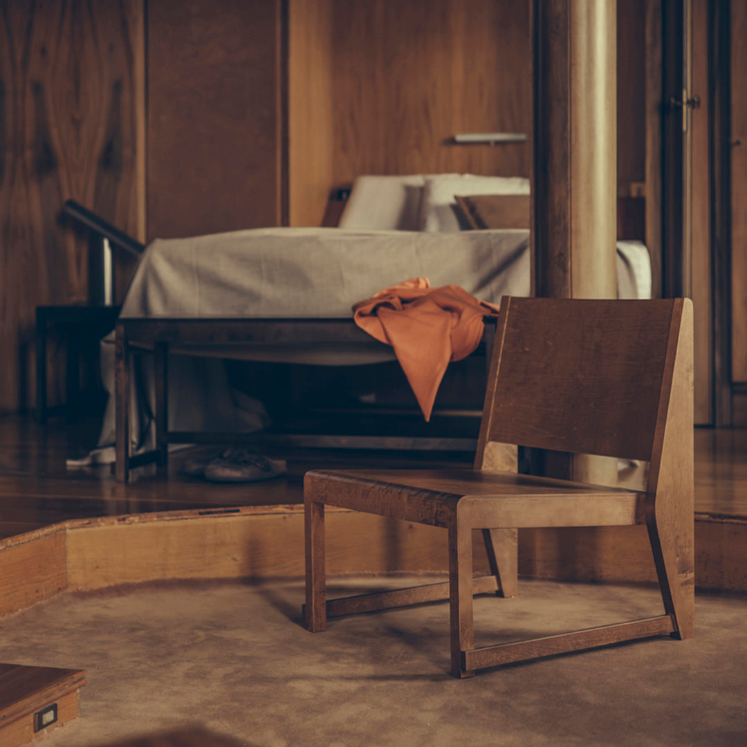 "Wooden chair with a minimalist design, featuring warm wood tones and an orange accent blanket in a cozy setting."