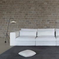 White modern sofa on a textured gray rug, with a neutral stone wall and minimalist lamp for a contemporary look.