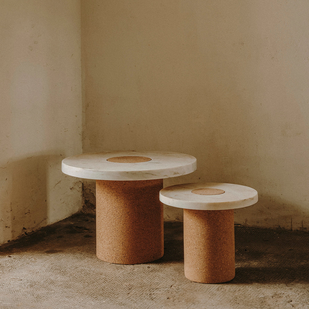 White circular tabletops with natural cork bases, featuring a minimalist design and warm, earthy tones.