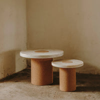White circular tabletops with natural cork bases, featuring a minimalist design and warm, earthy tones.