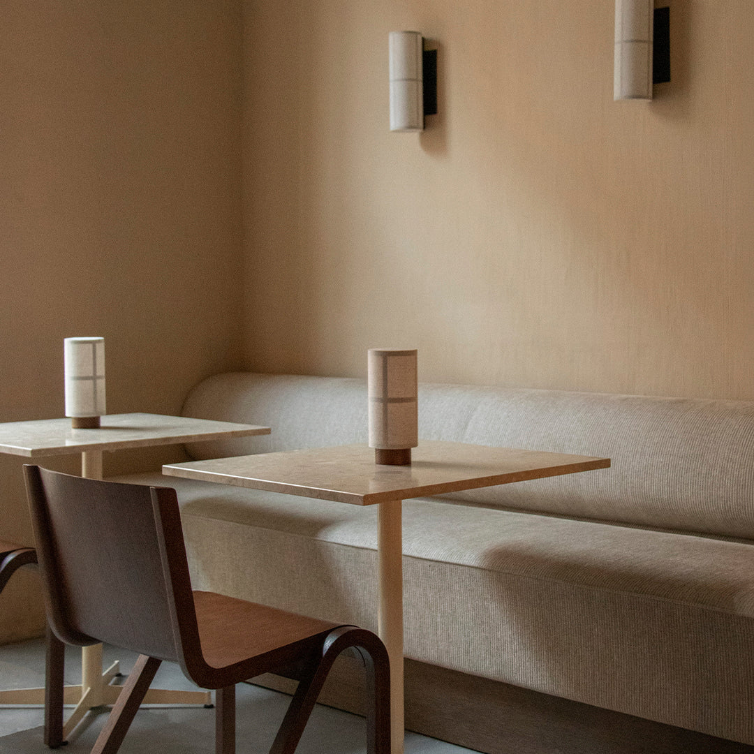Soft beige walls complement a minimalistic light wood table and warm-toned chair, with cylindrical vases adding elegant texture.