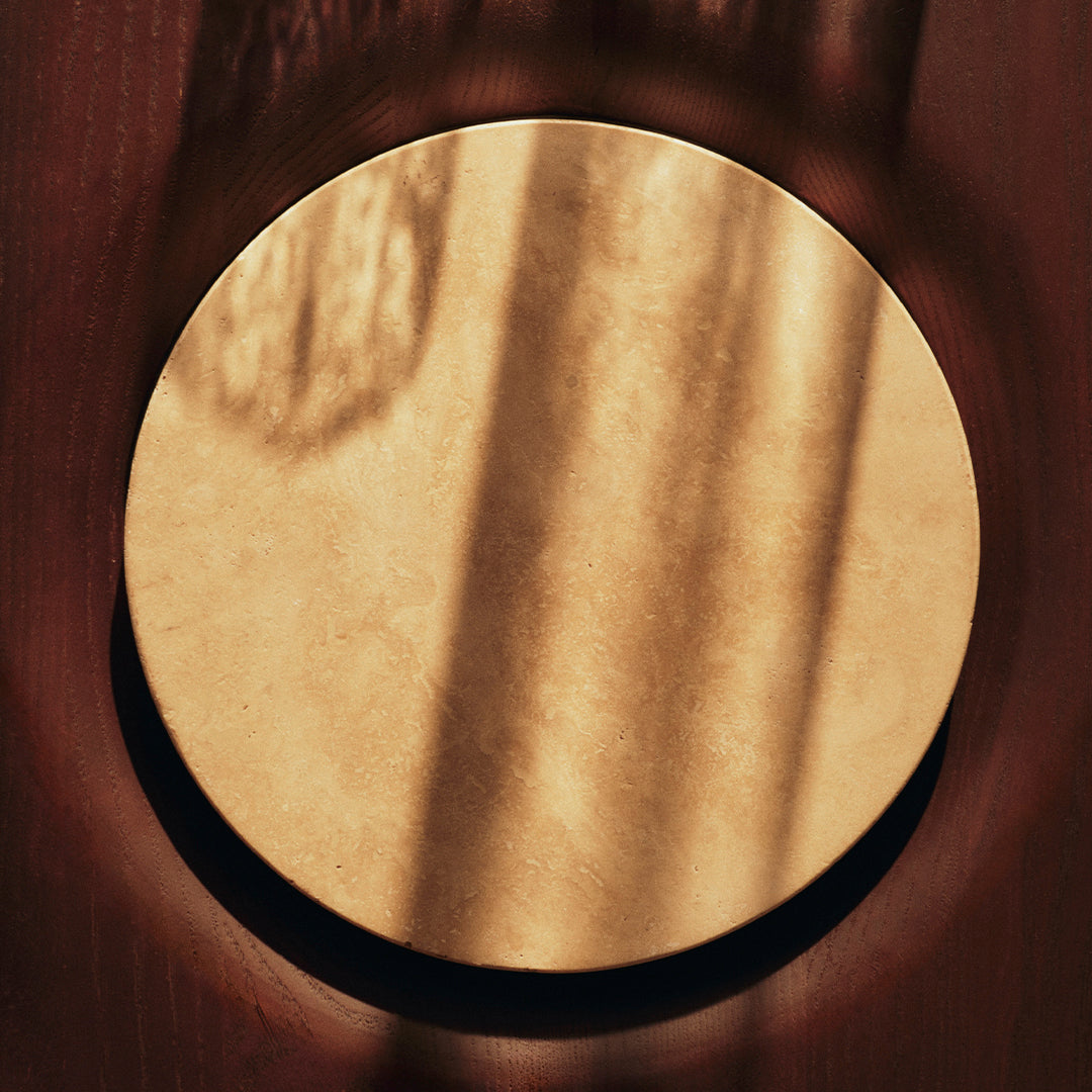 Round gold accent piece with a smooth finish, contrasted by a dark circular border, showcasing soft shadow patterns.