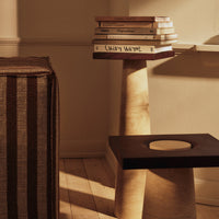 Striking two-tone side table with smooth wooden finish and solid black top, complemented by a striped sofa.