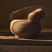 Beige textured armchair with a rounded design, featuring soft, curved lines and a cozy pattern. Ideal for modern decor.