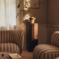 "Textured beige and cream striped armchair with a sleek black accent table in a sunlit room."