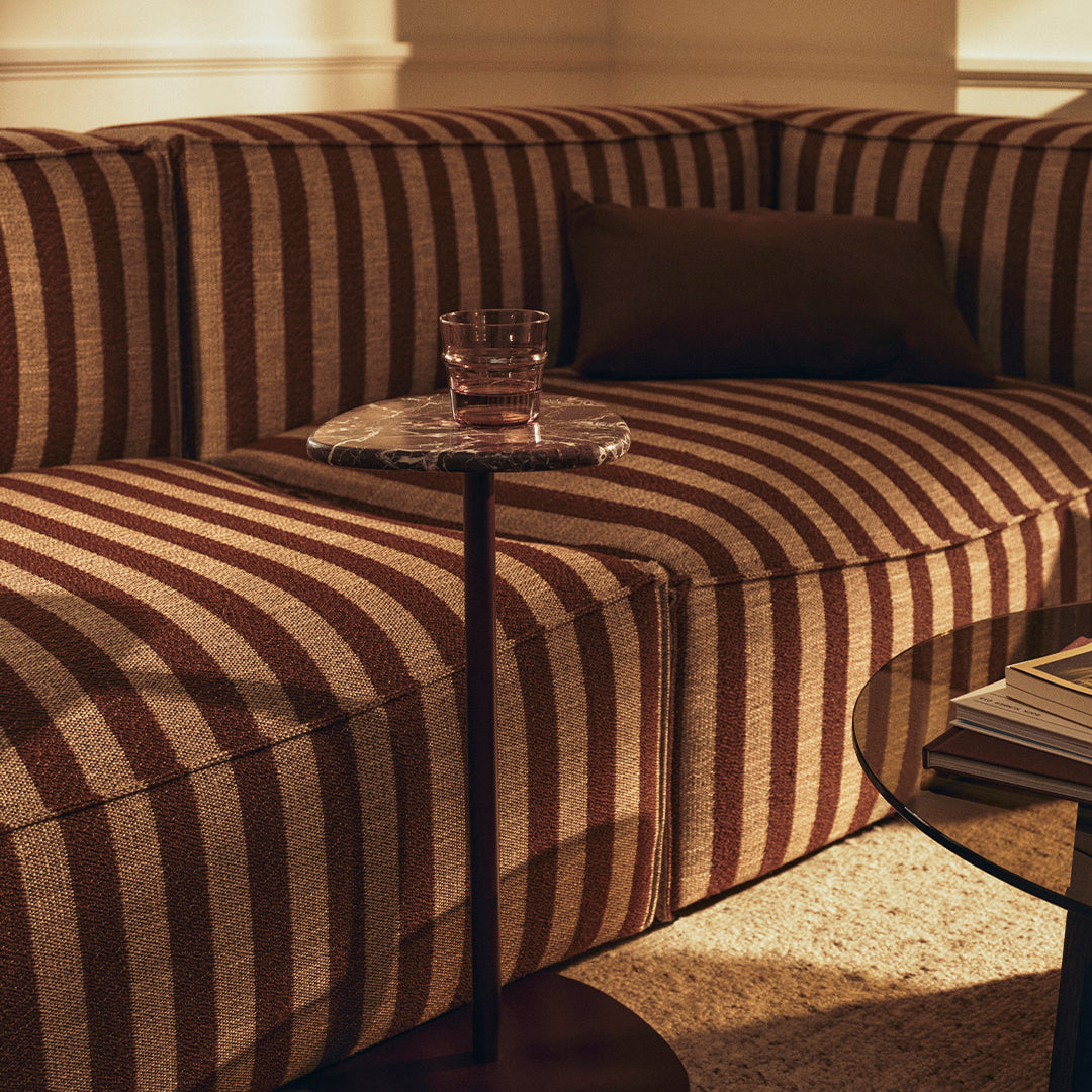 Striped brown and beige sofa with a modern aesthetic, complemented by a clear glass side table and earthy tones.