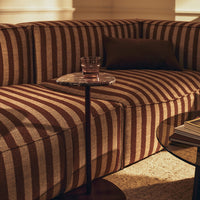 Striped brown and beige sofa with a modern aesthetic, complemented by a clear glass side table and earthy tones.