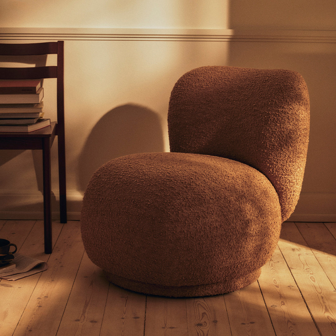 Textured brown chair with a modern rounded design, set against a warm, softly lit wooden floor.