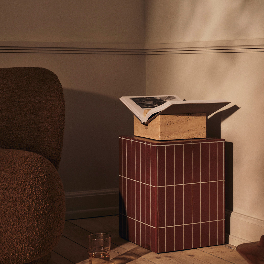 "Textured brown sofa and a red striped side table with a neutral-colored box and magazine on top."