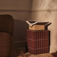 "Textured brown sofa and a red striped side table with a neutral-colored box and magazine on top."