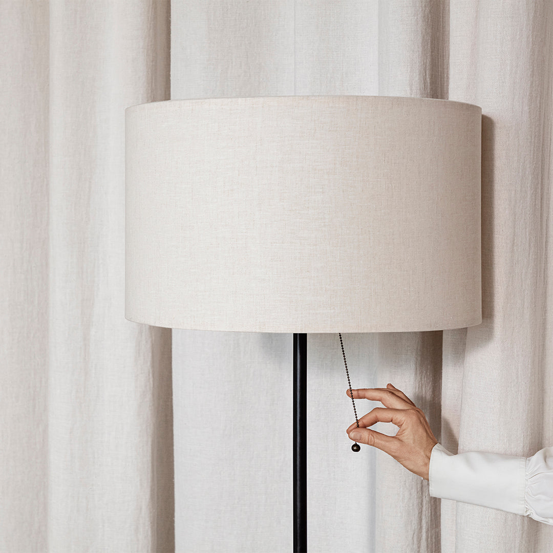 Beige linen lamp shade with black base, featuring a smooth, minimalist design against light curtains.