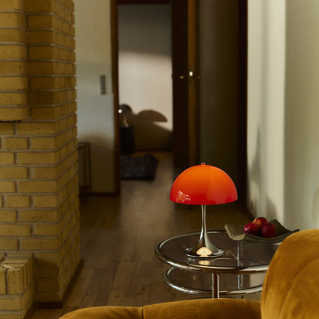 "Vibrant orange lamp with a smooth, rounded shade, contrasting against warm wood tones and soft beige walls."