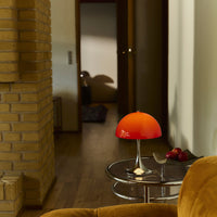 "Vibrant orange lamp with a smooth, rounded shade, contrasting against warm wood tones and soft beige walls."