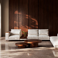 Modern white sectional sofa with brown wood accents against a dark wood wall, complemented by circular wooden coffee tables.
