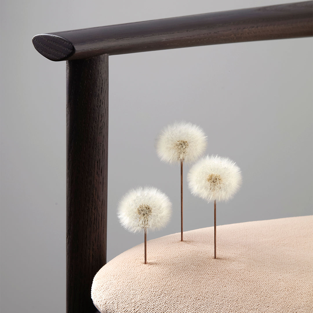 Three fluffy white dandelion-like decor pieces on a soft beige cushion with a dark wooden frame.