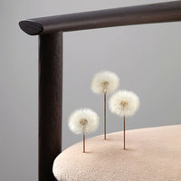 Three fluffy white dandelion-like decor pieces on a soft beige cushion with a dark wooden frame.