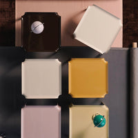 Colorful square plates in brown, cream, yellow, pink, and green with varied glossy finishes and playful designs.