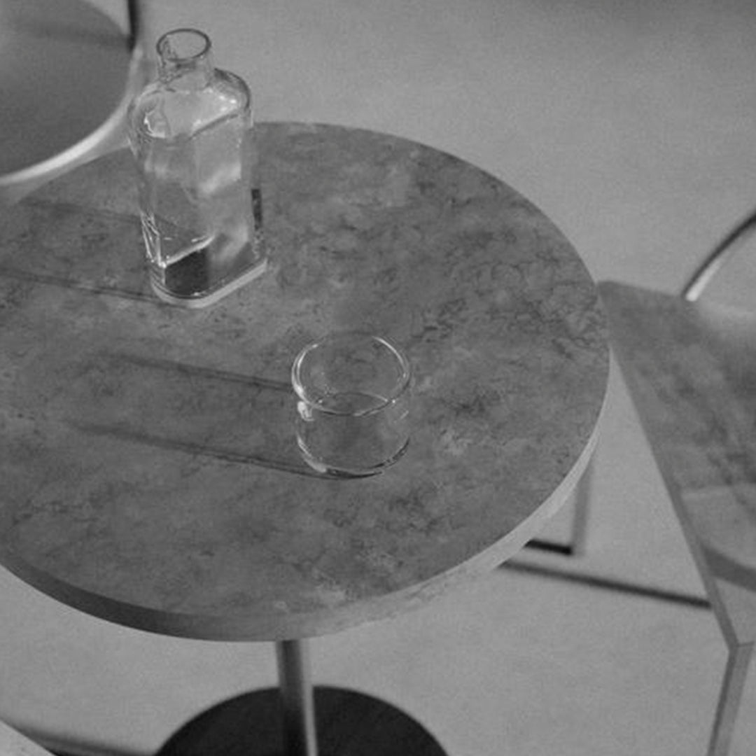 Gray marble round table with subtle veining, featuring a glass and bottle on a modern minimalist backdrop.