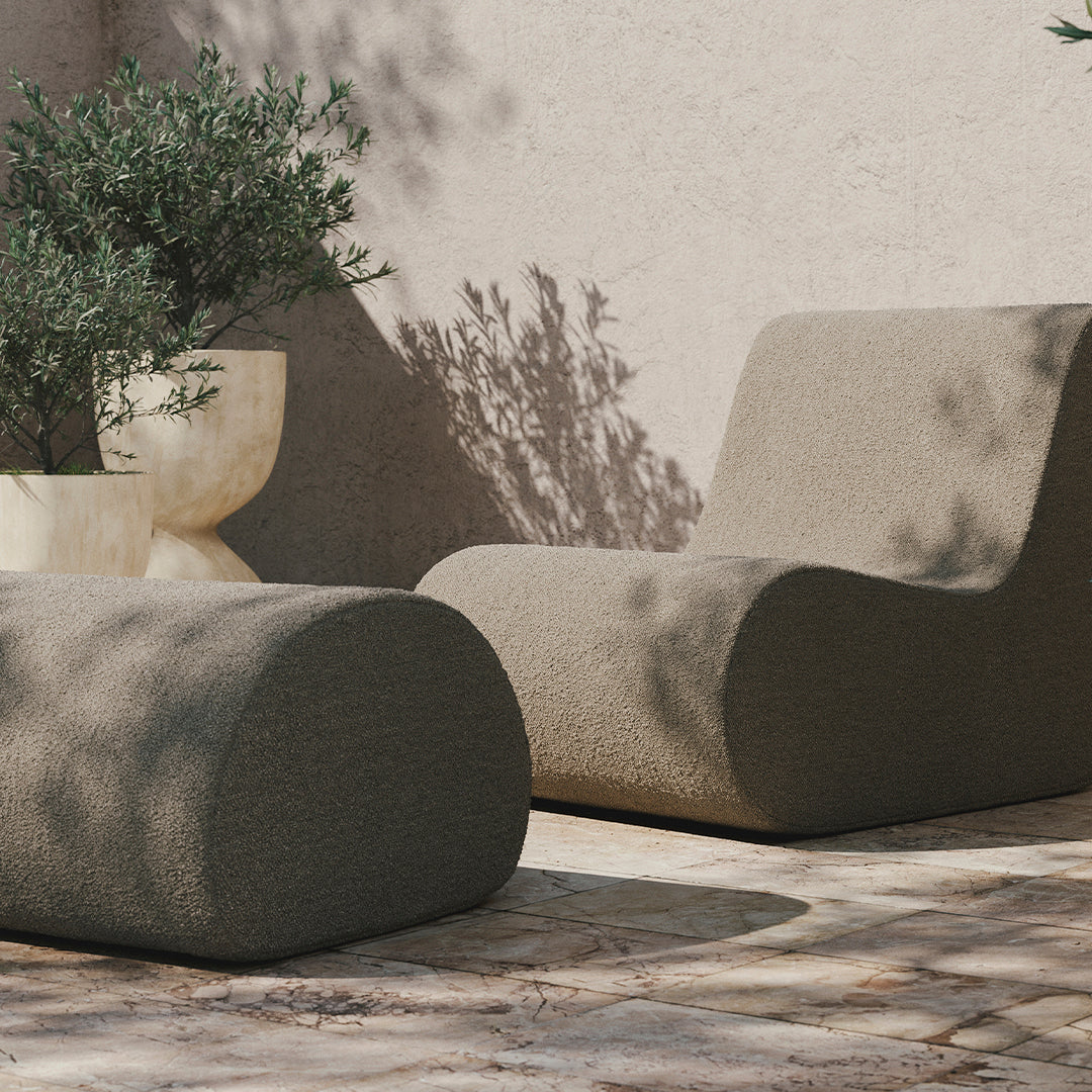 Soft beige lounge chair and ottoman with smooth, curved shapes, set against a neutral, textured background.