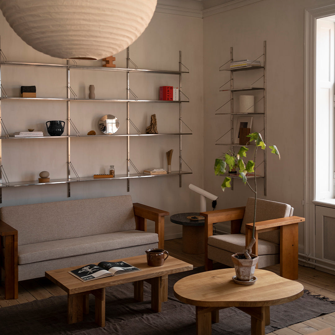 "Neutral beige sofa with light wood accents, paired with round and rectangular wooden tables in a minimalist setting."