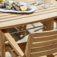 Natural wood table with slatted pattern, complemented by a light wooden chair, set outdoors with fresh seafood.