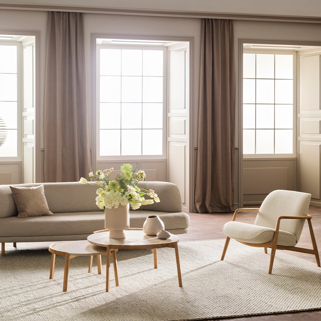 Light beige sofa with soft cream accents, natural wood furniture, and pastel floral arrangement in a minimalistic space.