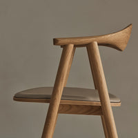 Beige padded seat with natural wood legs and a smooth curve, set against a muted gray background.