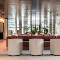 Modern lounge area with a rust-colored sofa, beige cylindrical tables, and glossy metallic accents reflecting greenery.