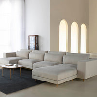Light gray sectional sofa with smooth fabric and minimalist design, paired with a dark rug and elegant décor accents.