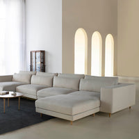 Light gray sectional sofa with a smooth, minimalist design, complemented by a dark rug and soft natural lighting.
