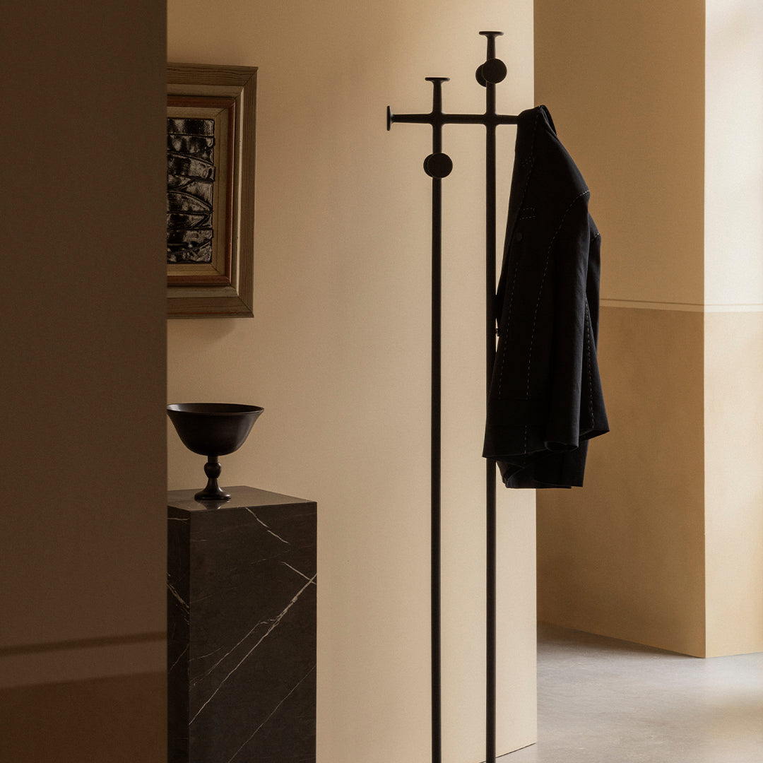 Sleek black coat rack against warm neutral walls, highlighting modern minimalist design and subtle shadows.