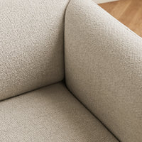 Beige textured fabric close-up, showcasing a subtle pattern on a modern couch corner. Warm, neutral tones.