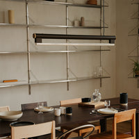 "Stylish black and brushed metal pendant light above a wooden dining table with neutral dishes and décor."