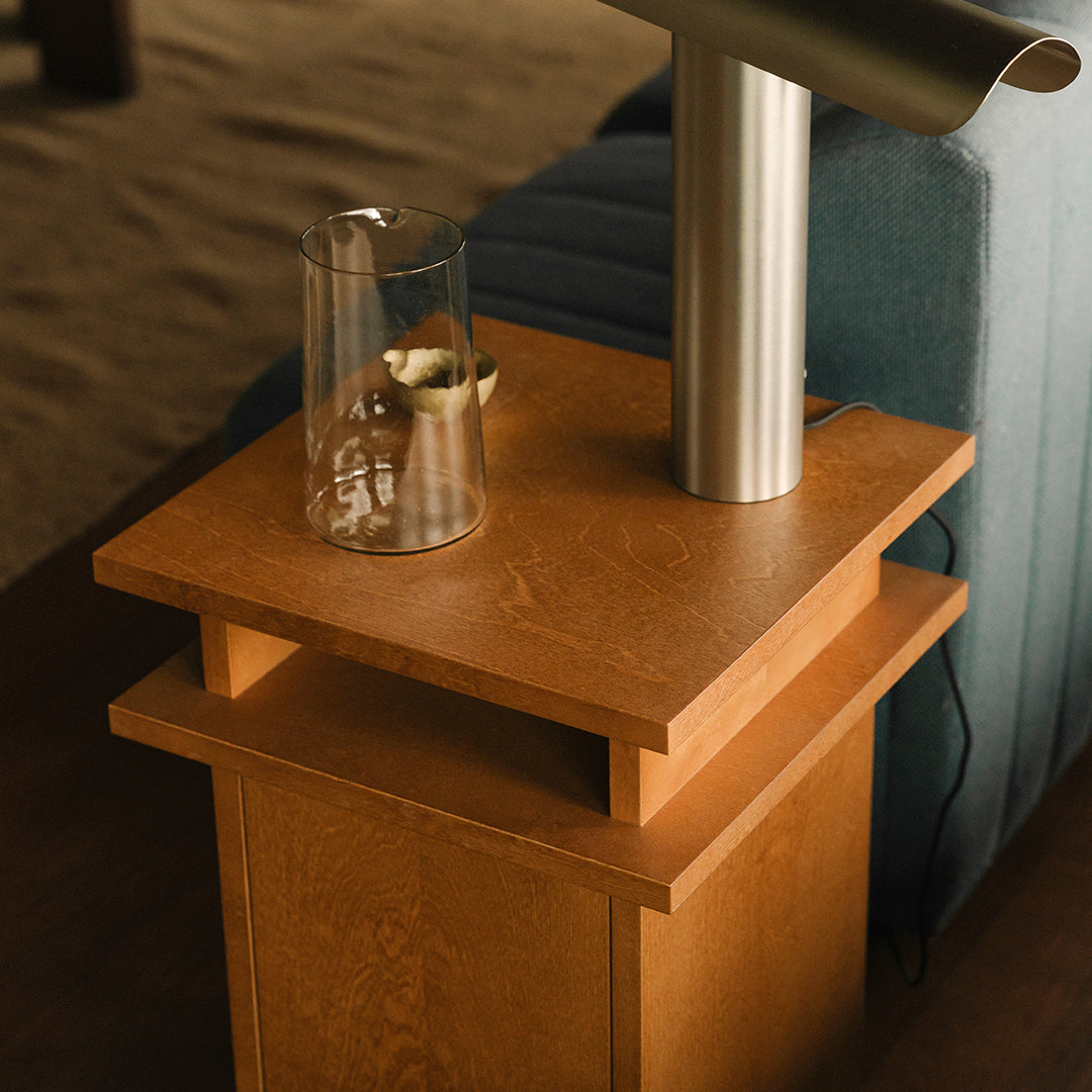 Light wooden nightstand with a smooth surface, complemented by a sleek silver lamp and a glass vase.
