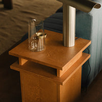Light wooden nightstand with a smooth surface, complemented by a sleek silver lamp and a glass vase.
