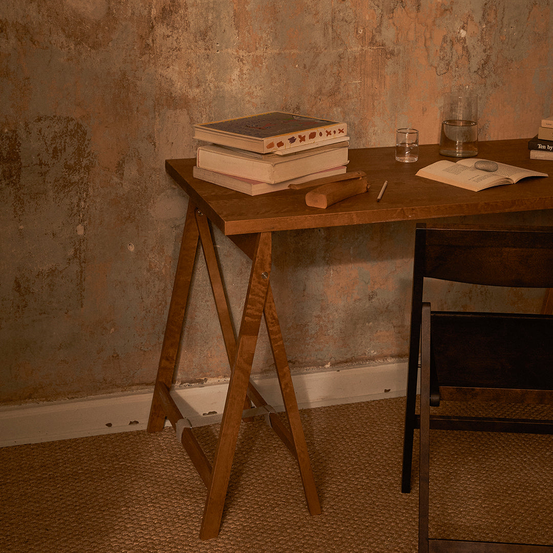 Wooden desk with a rich brown finish, surrounded by textured pale pink and muted gray wall, featuring a woven beige rug.