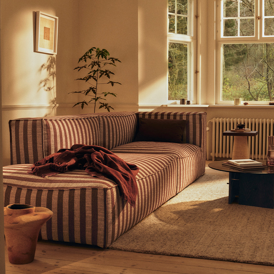 Striped sofa in warm earthy tones with deep red throw, enhancing a cozy, inviting living space.