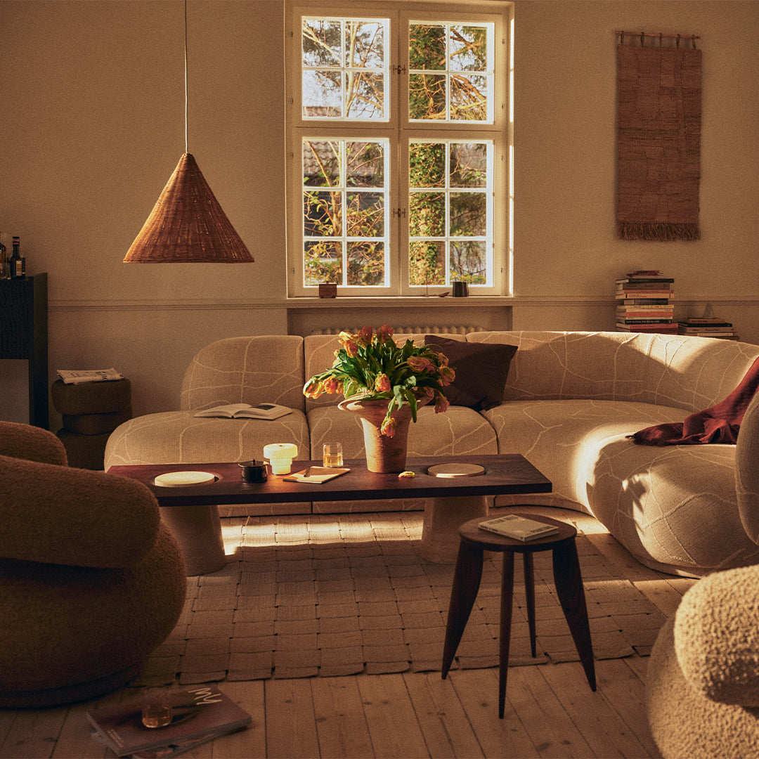Cozy living room featuring beige curved sofas, warm wood accents, and soft earthy tones illuminated by natural light.
