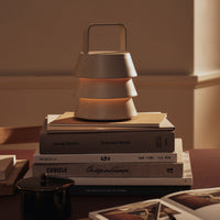 Modern lamp with a stacked design in soft beige and warm gray hues, accentuated by gentle lighting, placed on books.