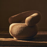 Beige boucle armchair with smooth, rounded shapes, casting soft shadows in warm, natural lighting.