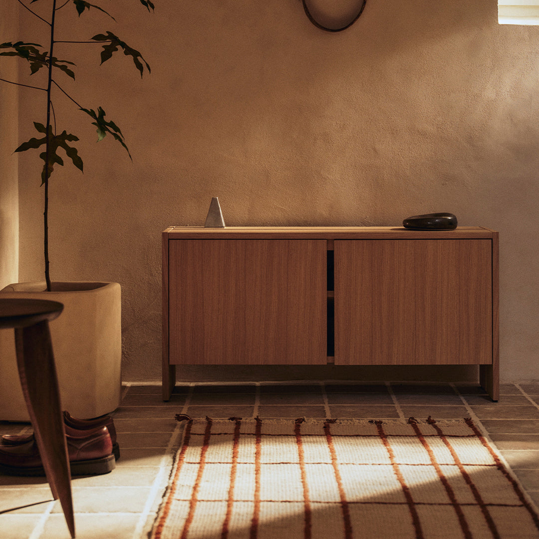 Natural wood cabinet with warm tones, paired with a textured cream and rust-striped rug on a tiled floor.
