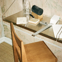 Wooden chair with a natural finish, metallic desk surface, glass and paper accessories in a textured beige and green background.