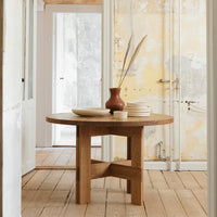 Round wooden table with a natural finish, complemented by a terracotta vase and neutral plate set.