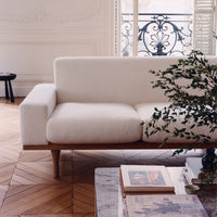 Minimalist white sofa with a textured fabric, complemented by light wood legs and surrounded by a neutral decor.