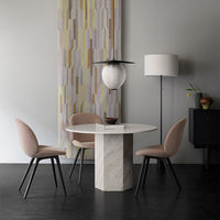 Modern round dining table with a marble base, surrounded by soft pink chairs and a geometric patterned wall hanging.