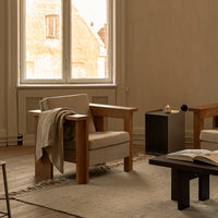 Light beige armchair with wooden frame, complemented by a soft, neutral throw and a textured cream rug.