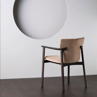 Beige upholstered chair with dark wooden frame, set against a minimalist wall with a circular cutout.