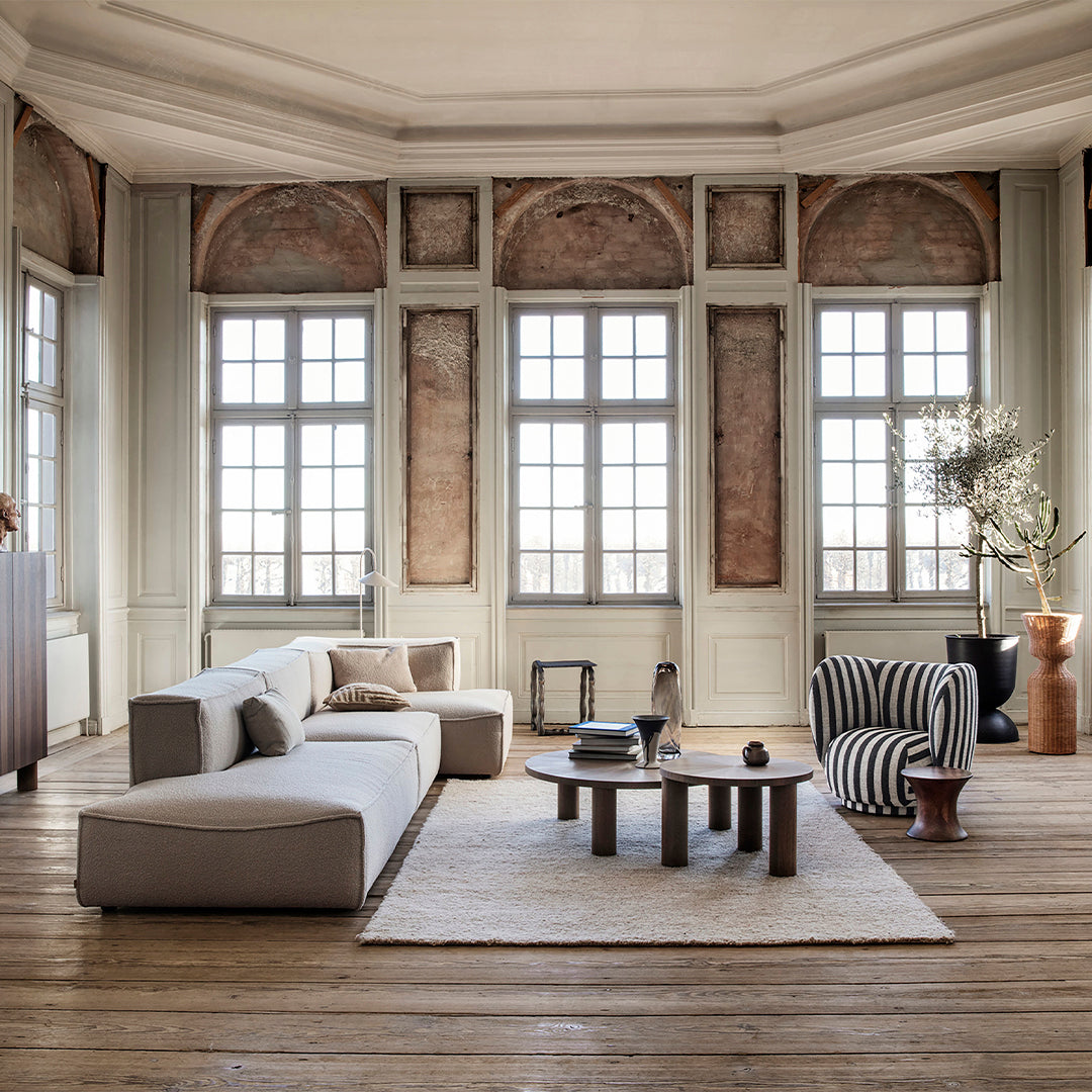 Modern living room featuring a neutral sofa, striped chair, and earthy tones against a light wooden floor.