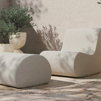 Modern beige lounge chairs with smooth, rounded shapes against a textured stone patio and lush greenery.
