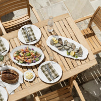 "Wooden table set with white plates, green-check napkins, colorful veggie platter, and seafood on a sunny day."